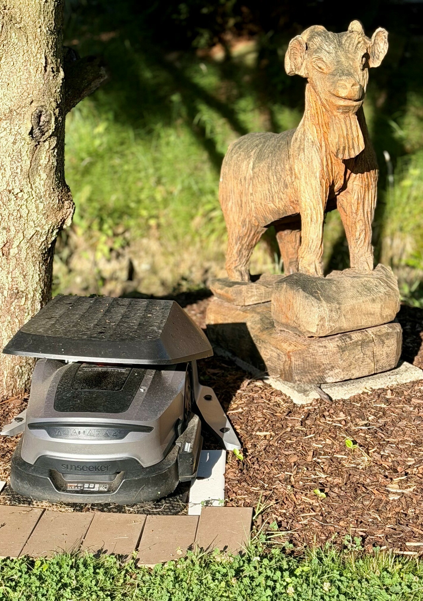 Gretel in der Ladestation unter den Augen von Hennes Mähroboter Gretel in der Ladestation neben der Hennes-Figur im Park des Waldhotels